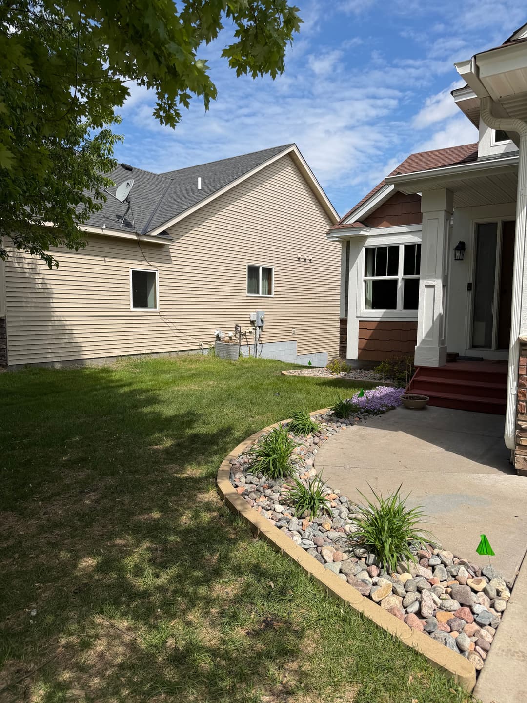 Side view of a home with landscaped garden, featuring a path and vibrant plants under a blue sky.