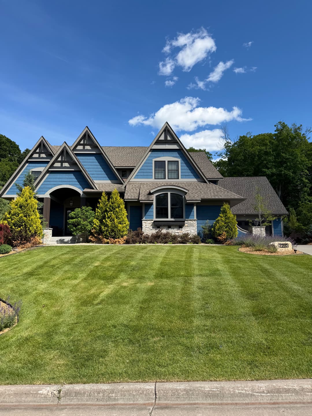 Blue modern house with triangular roof, green lawn, and landscaped garden under clear sky.